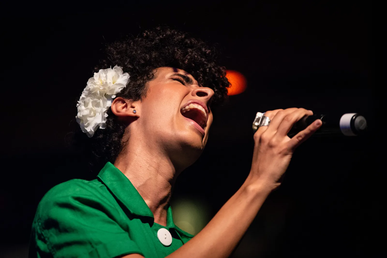 Cantora em roupa verde canta sob luz de palco.